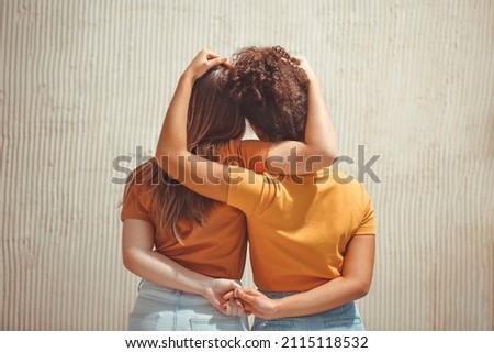 Strong female friendship. Rear view two teen girls best friends holding hands behind back and hugging while standing in front of beige wall outdoors Royalty-Free Stock Photo #2115118532