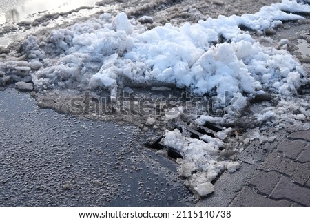 part of street in city, drainage runoff, pavement after heavy snowfall, wet snow melts, slush and mud impede movement of pedestrians and vehicles, concept traffic safety, work of public utilities Royalty-Free Stock Photo #2115140738