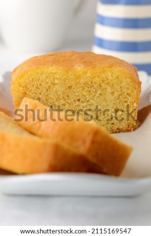 Home baked cake for afternoon tea,  cut into slices on a white rectangular plate with blue and white striped cornishware style jug in the background