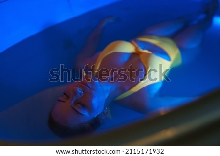 Beautiful woman floating in tank filled with dense salt water used in medical therapy. Royalty-Free Stock Photo #2115171932