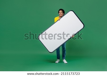 Full size young black man 20s wears yellow waterproof raincoat outerwear hold in hand big white empty blank mobile cell phone for promotional content isolated on plain green background studio portrait