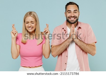 Young couple two friends family man woman in casual clothes waiting for special moment, keeping fingers crossed, prayer gesture together isolated on pastel plain light blue color background studio. Royalty-Free Stock Photo #2115173786