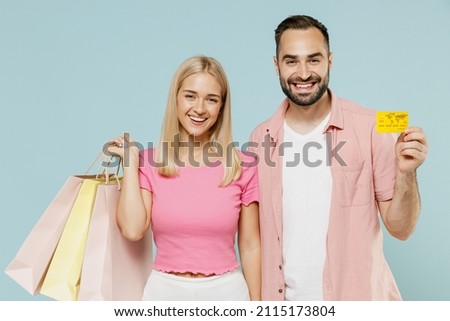 Young couple two friends family man woman in casual clothes hold package bags with purchases after shopping credit bank card together isolated on pastel plain light blue background studio portrait.