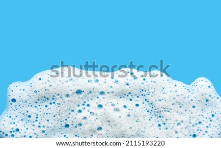 White foam soap sud on blue background. Foam bubbles of detergent fluid gel. Royalty-Free Stock Photo #2115193220