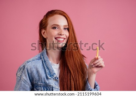 cute red long foxy haired ginger woman holding packaging cardboard box with french fries in pink studio