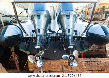 Two outboard motors at the stern of a motorboat resting on wooden blocks in dry dock. Royalty-Free Stock Photo #2115206489