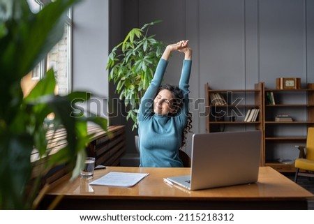 Happy businesswoman warming up body and muscles at workplace, feeling satisfied with work done, smiling female employee resting from computer screen. Well-being, productivity and happiness at work Royalty-Free Stock Photo #2115218312