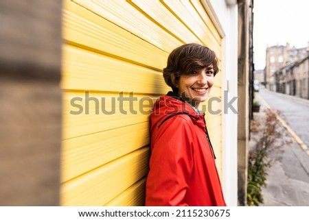 Portrait of an attractive young female wearing a red raincoat with a yellow door in the background