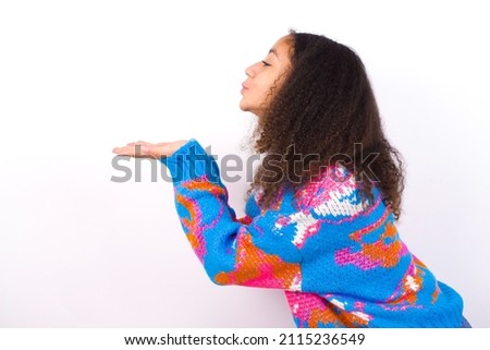 Profile side view view portrait of attractive beautiful teenager girl wearing colorful sweater over white background sending air kiss