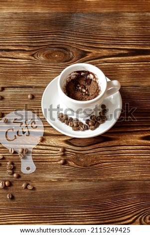 Top view of ceramic cup of hot cappuccino coffee latte with drawing picture of cafe sign plastic stencil, cinnamon or cocoa on milk foam, coffee beans on wooden table, copy space.
