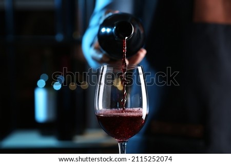 Bartender pouring red wine from bottle into glass indoors, closeup Royalty-Free Stock Photo #2115252074