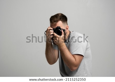 Young bearded man photographer takes images with dslr camera isolated on white background. Professional freelance work, hobby and active lifestyle concept.