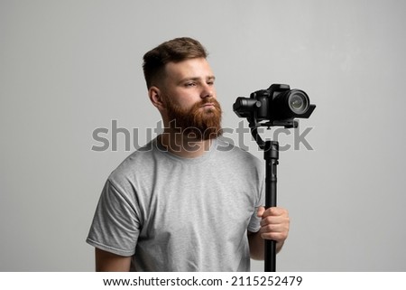 Bearder proffesional cinematographer with 3-axis gimbal and video camera on white background. Filmmaking, videography, hobby and creativity concept.