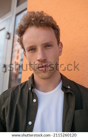 Close up portrait of young handsome pensive  man wearing stylish shirt looking at camera standing on the street near orange background. Fashion model posing for pictures outdoors 