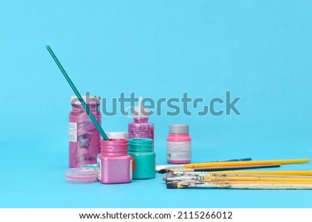 Group of used brushes and paint pots on blue background.