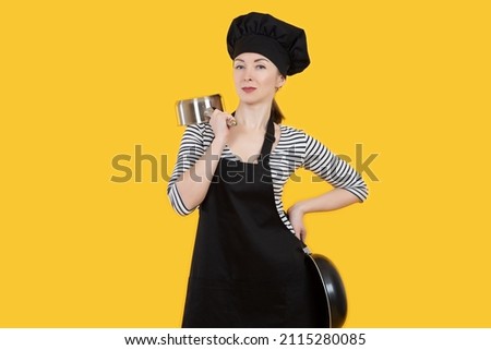 Chef with frying pans. Confident restaurant chef. Woman working in cafe. Girl in cook uniform. Concept of career in catering. Woman owner of restaurant on yellow background. Professional cook
