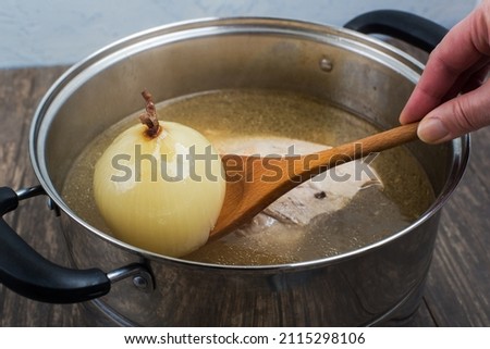 Meat broth in a saucepan and a boiled onion on a wooden spoon.