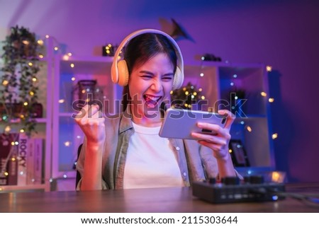 Excited Young Asian woman playing an online game on a smartphone with fists clenched celebrating victory expressing success.