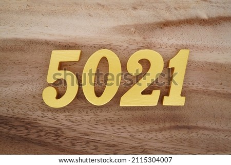 Wooden Arabic numerals 5021 painted in gold on a dark brown and white patterned plank background.