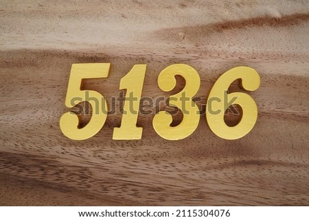 Wooden Arabic numerals 5136 painted in gold on a dark brown and white patterned plank background.
