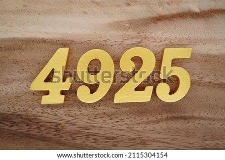 Wooden Arabic numerals 4925 painted in gold on a dark brown and white patterned plank background.