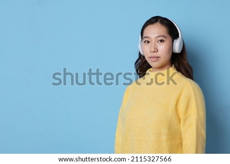 Studio photo with blue background of a young asian woman with wireless headphones facing the camera