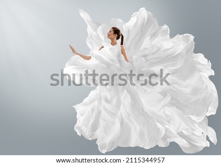 Fashion Model in Creative Pure White Dress as Cloud. Woman in Long Silk Gown with Chiffon Fabric flying on Wind over Light Gray Background. Art Fantasy dancing Girl Royalty-Free Stock Photo #2115344957