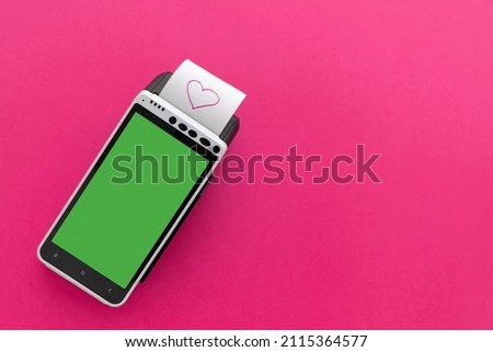 Credit card POS terminal with printed reciept with a pink heart picture on a pink background with a blank space. Happy Valentine's Day shopping idea