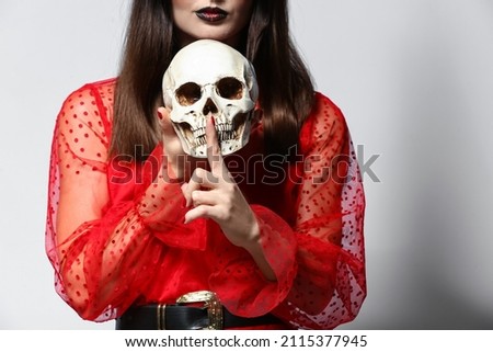 Young witch with skull on light background
