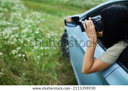 Woman photographer sitting in the car and photographing a flower field landscape, travel female take photo, space for text.