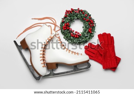 Ice skates with Christmas wreath and gloves on light background