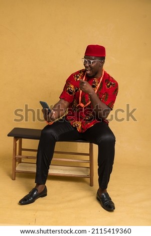 Igbo Traditionally Dressed Business Man Sitting Down and Staring at Phone and Joyful