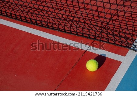 Tennis ball next to the net of a red hard surface tennis court. Racket sports concept.
