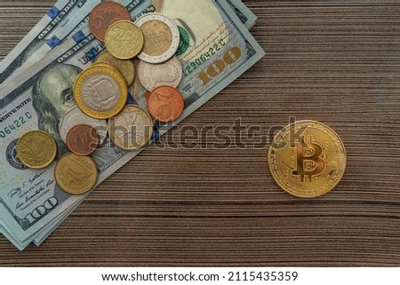 Top view of a bitcoin lying next to a stack of dollars and coins on the table. Investing in currency or cryptocurrency is the choice of the future.