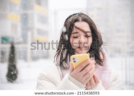 Portrait of a teenage girl outdoors with a smartphone in snowy winter weather.