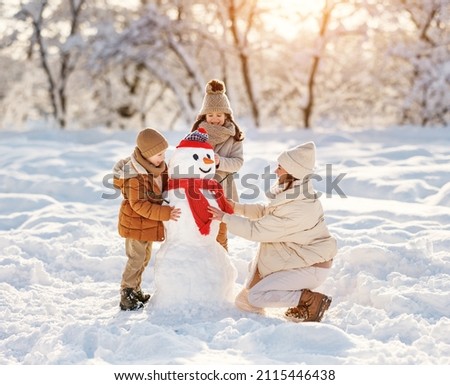 happy family mother and children boy and girl make a snowman and have fun on a winter walk in the park