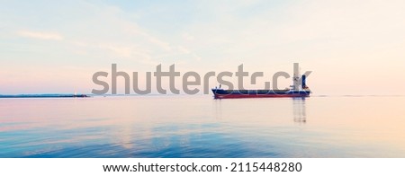 Large cargo ship sailing in the Baltic sea at sunset. Soft golden sunlight. Concept seascape. Panoramic view from the sailing boat. Freight transportation, nautical vessel, logistics Royalty-Free Stock Photo #2115448280