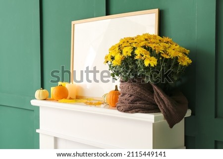Closeup view of beautiful Chrysanthemum flowers and blank photo frame on fireplace near color wall