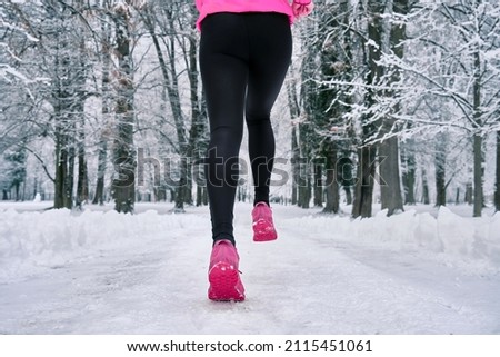 Running woman, girl runner on snow in park in winter sunny day. Female in pink sportswear jacket fitness training outdoors. Run, Sport concept, leisure and freedom.