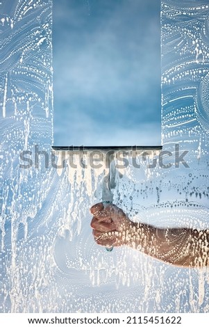 Window cleaner using a squeegee to wash a window with clear blue sky Royalty-Free Stock Photo #2115451622
