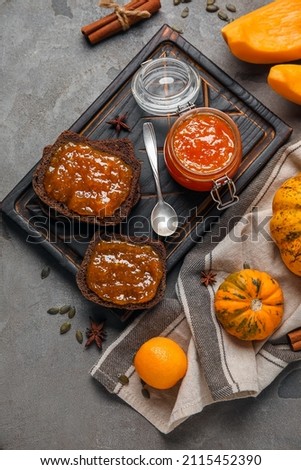 Jar of sweet pumpkin jam with orange and toasts on grey background