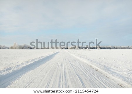 Country road through the snow-covered fields, rural area. View from car. Snow drifts. Europe. Nature, christmas vacations, remote places, winter tires, dangerous driving concept Royalty-Free Stock Photo #2115454724