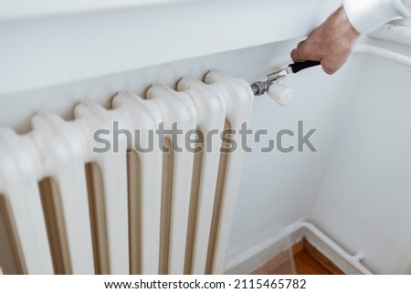 Plumber fixing radiator with wrench. Hands with adjustable wrench repairs a heating radiator. Technical check-up. Male hands hold a flat wrench by which they unscrew the temperature control valve.