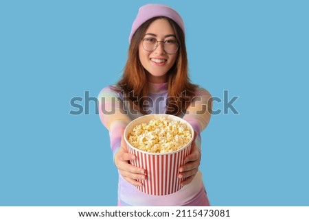 Stylish young Asian woman with tasty popcorn on blue background
