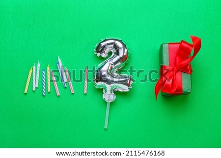 Composition with silver balloon in shape of figure 2 on green background