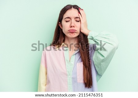 Young caucasian woman isolated on green background tired and very sleepy keeping hand on head.
