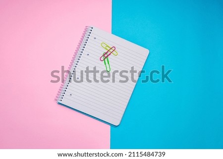 Notebook with paperclips on a two-tone pink and blue background