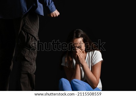 Aggressive man and scared young woman on dark background. Violence concept