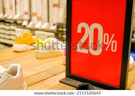 20 sales sign card in clothes store close-up across shelves with shoes and sneakers. Sales, discount, black Friday, cyber Monday, season sales concept. retail business	
