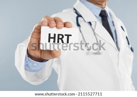 Doctor holding card with abbreviation HRT on light grey background, closeup. Hormone Replacement Therapy Royalty-Free Stock Photo #2115527711
